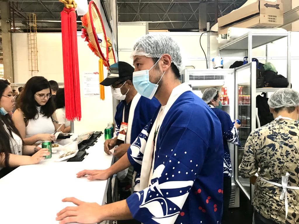 Voluntários servindo pratos na cozinha do estande da Yamagata em 2022