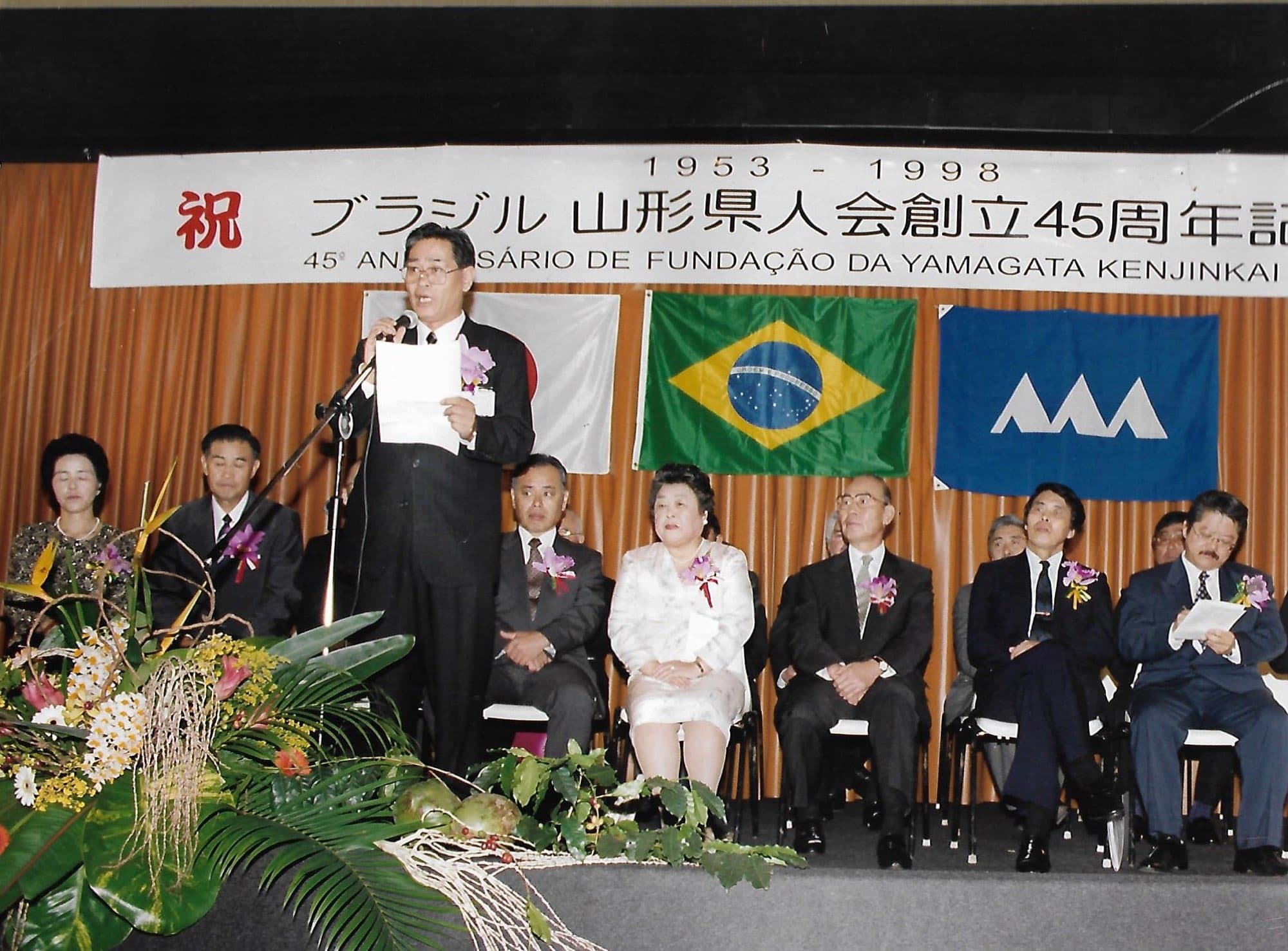 Cerimônia dos 45 anos da Associação Yamagata Kenjin do Brasil, em 1998, com as bandeiras do Japão, do Brasil e da província de Yamagata
